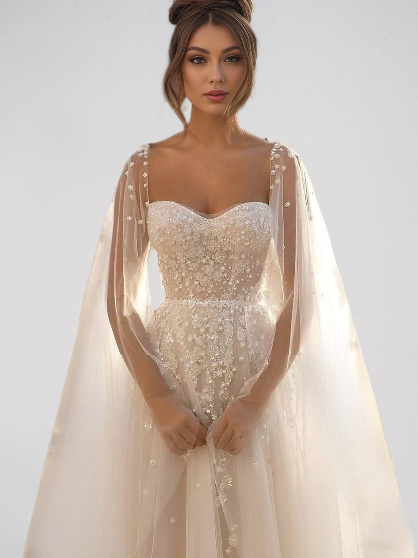 Bride in sheer bridal gown with pearl and lace accents on top and cape sleeves