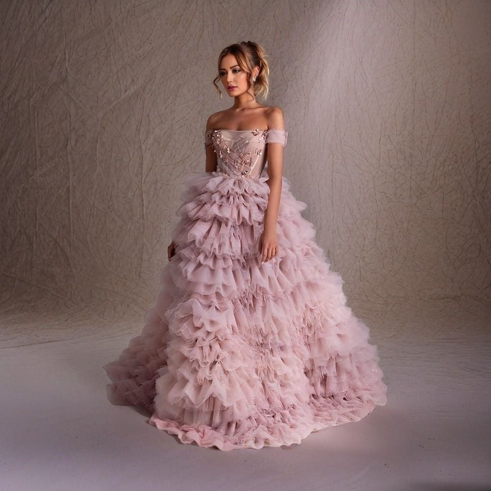 Model in Pink Tiered Evening Gown: A full-length shot of a model wearing the HARVIE dress, showcasing the tiered A-line silhouette in a soft pink color.