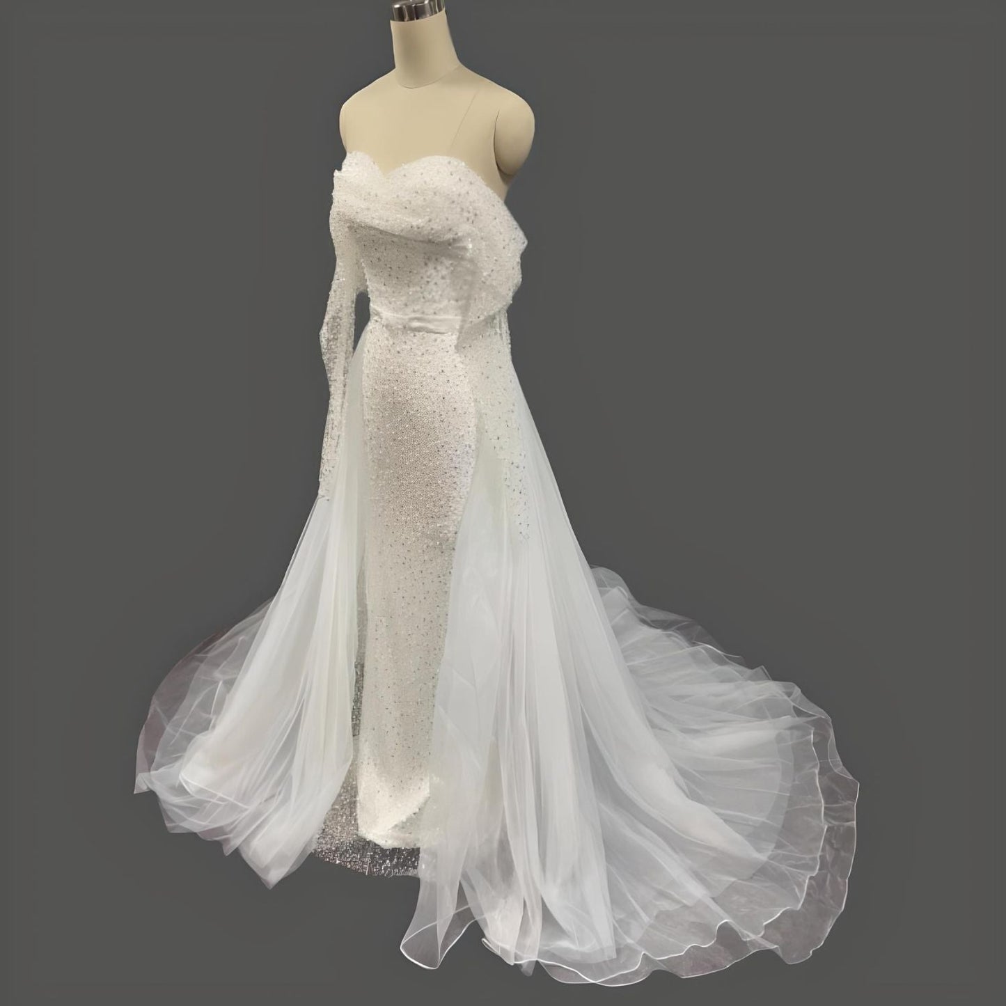 Sequined mermaid dress on manequin featuring a ruched bodice, off-the-shoulder sleeves, and a removable tulle overskirt.