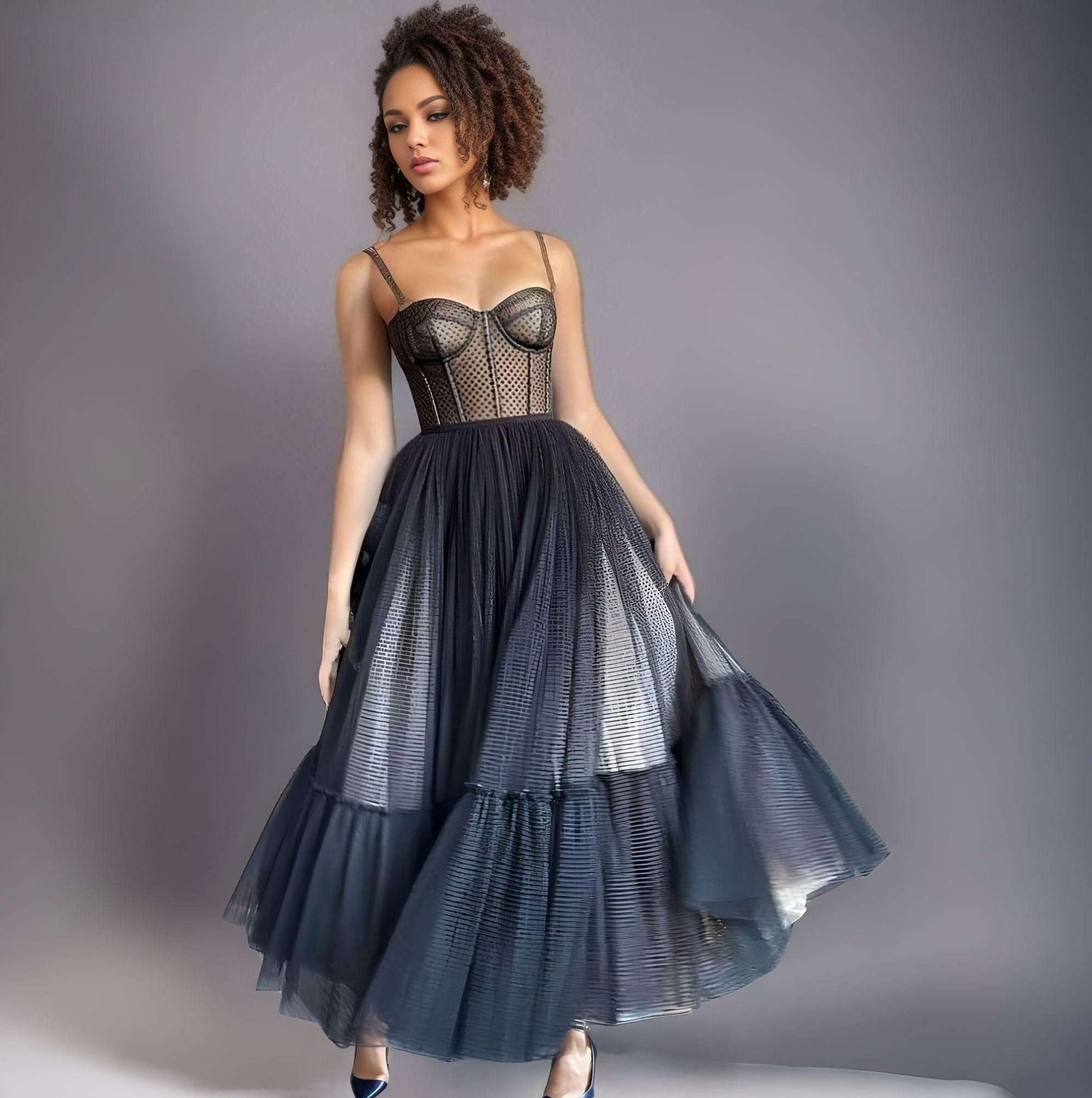 Model in a tea-length black prom dress with dotted tulle, spaghetti straps, and a corset top, perfect for special occasions.