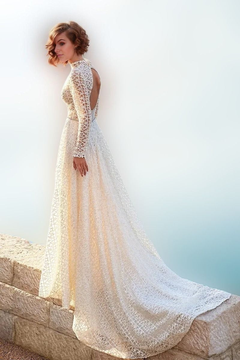 Woman in stunning boho-style bridal gown featuring glittered lace tulle, an open back with and waist crystal sash, with graceful A-line silhouette.