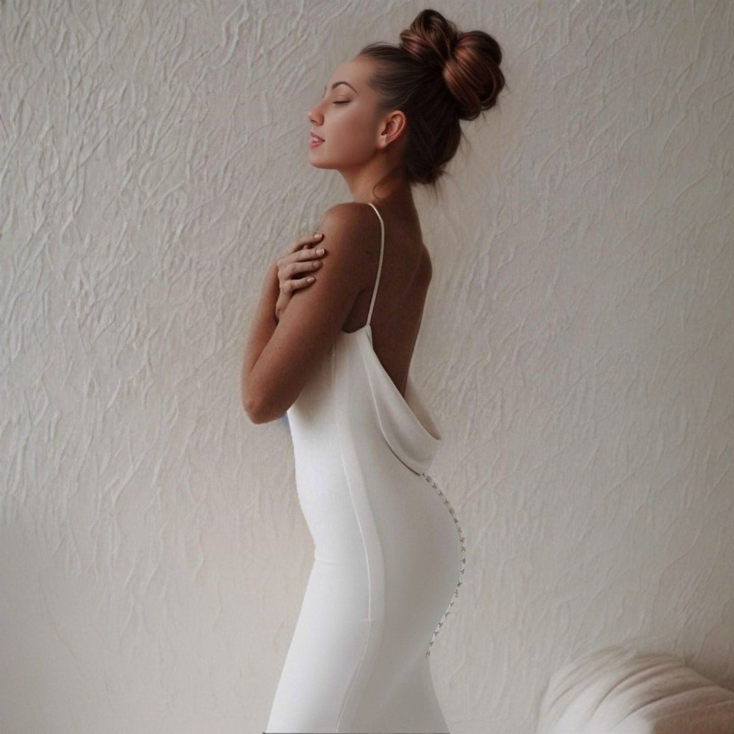 Woman from side wearing a simple mermaid wedding gown with a backless design and plunging fabric on lower back with back buttons.