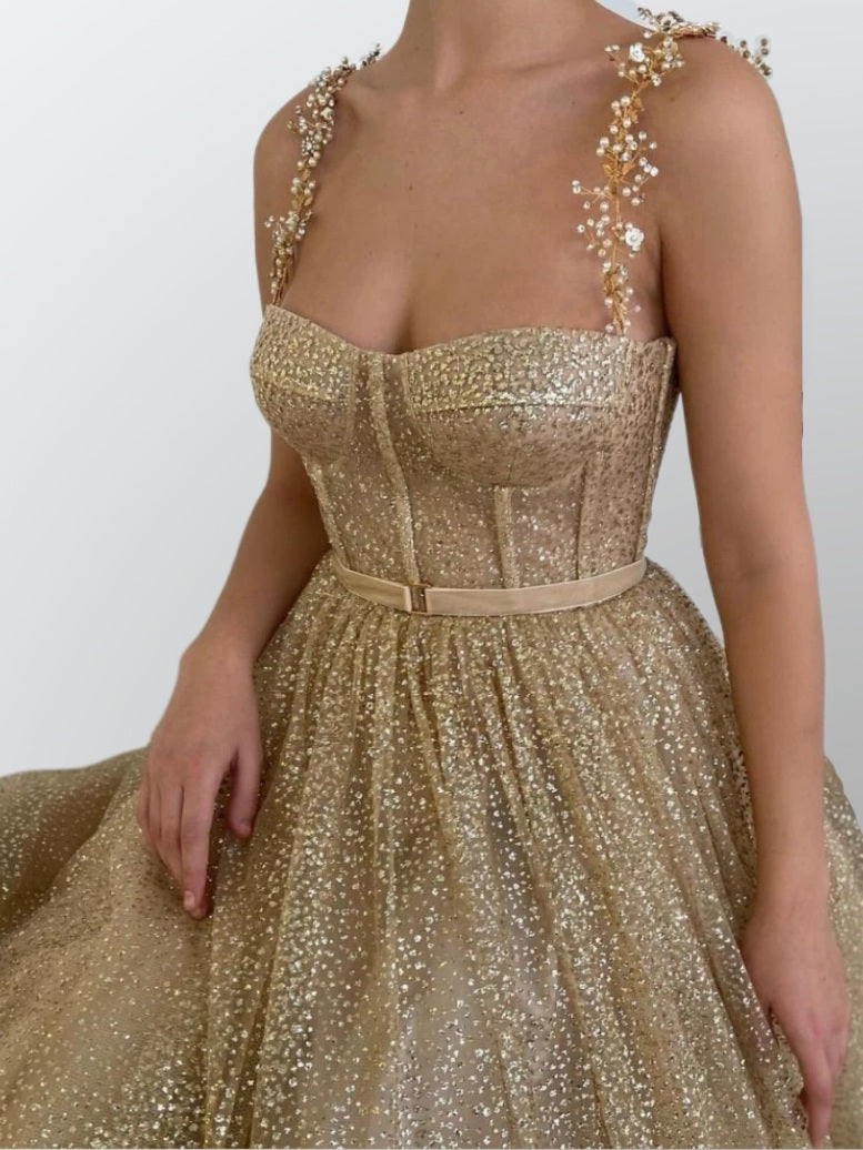 Woman in a gold glitter A-line dress featuring a fitted bodice, tea-length skirt, and beaded spaghetti straps, perfect for formal occasions.