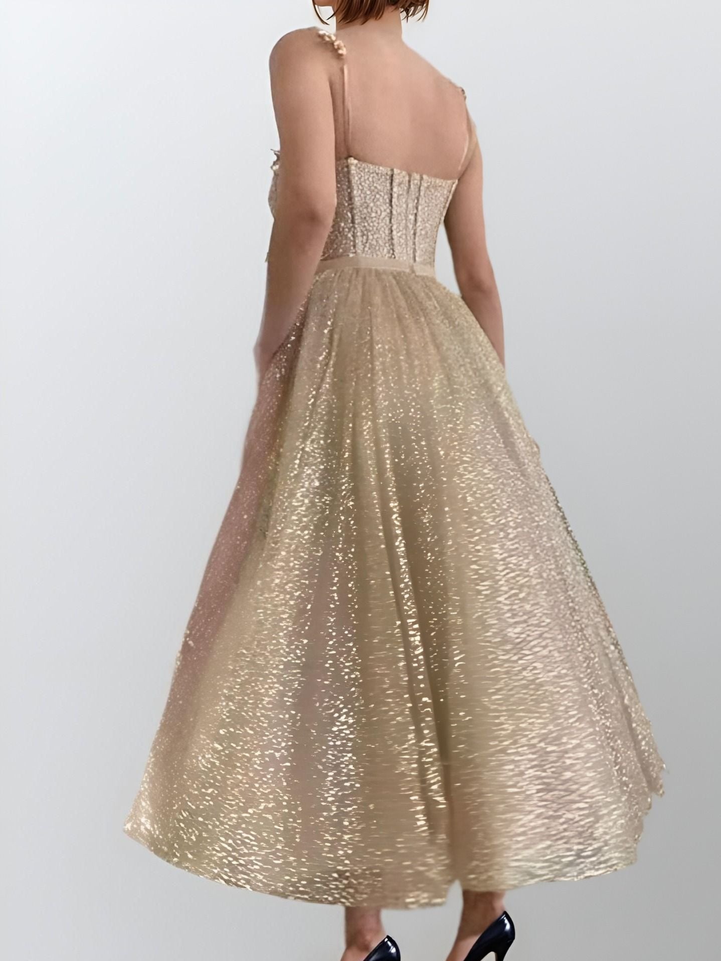 Woman wearing a glittery gold tea-length dress with a fitted bodice, beaded straps, and pockets, designed for a sparkling and stylish entrance.