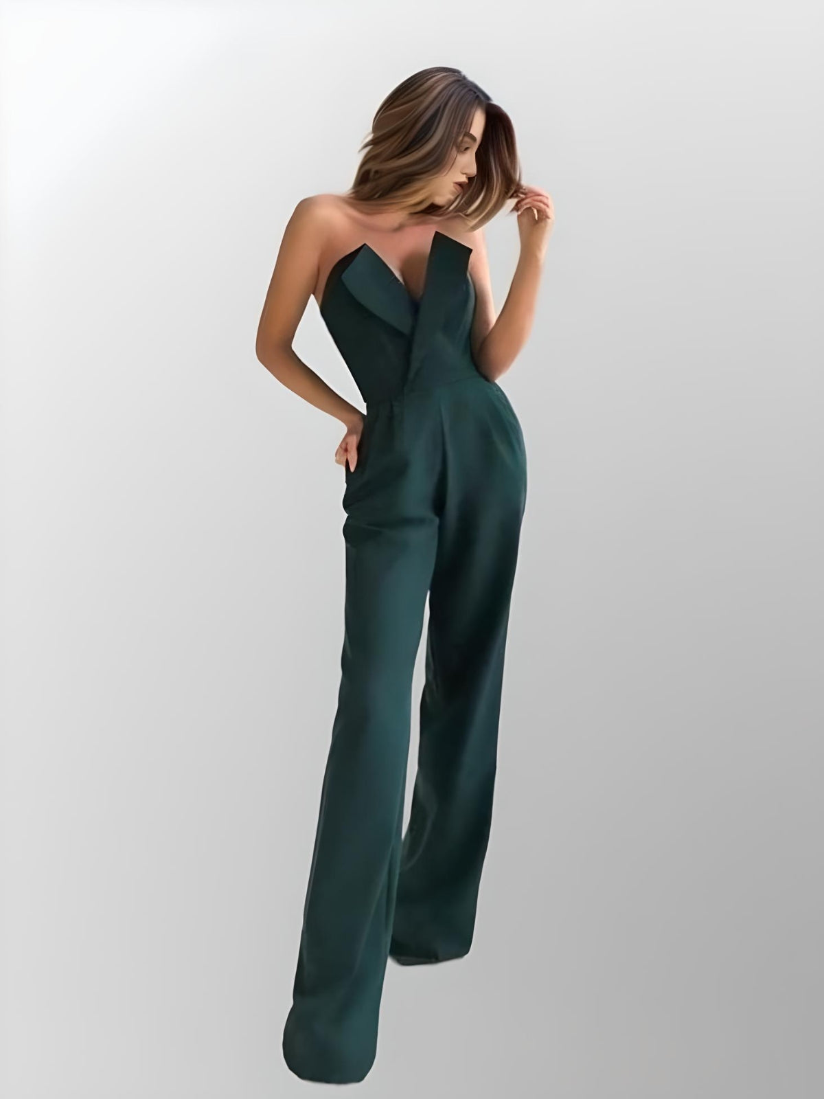 Model showcasing a dark emerald green sleek jumpsuit with a deep V-neck and asymmetrical neckline, featuring pockets.