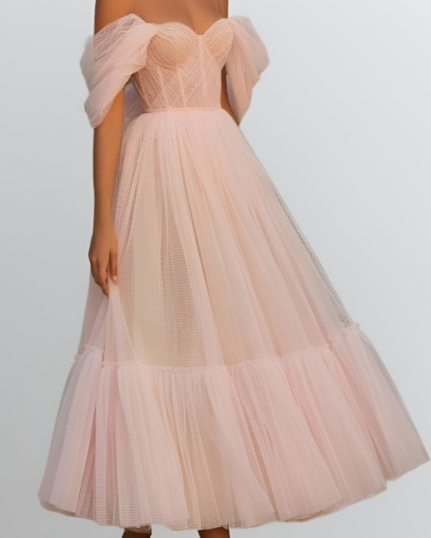 Woman wearing a blush pink formal dress with a pleated bodice, off-shoulder layered sleeves, and a tiered A-line skirt, perfect for prom or special occasions.