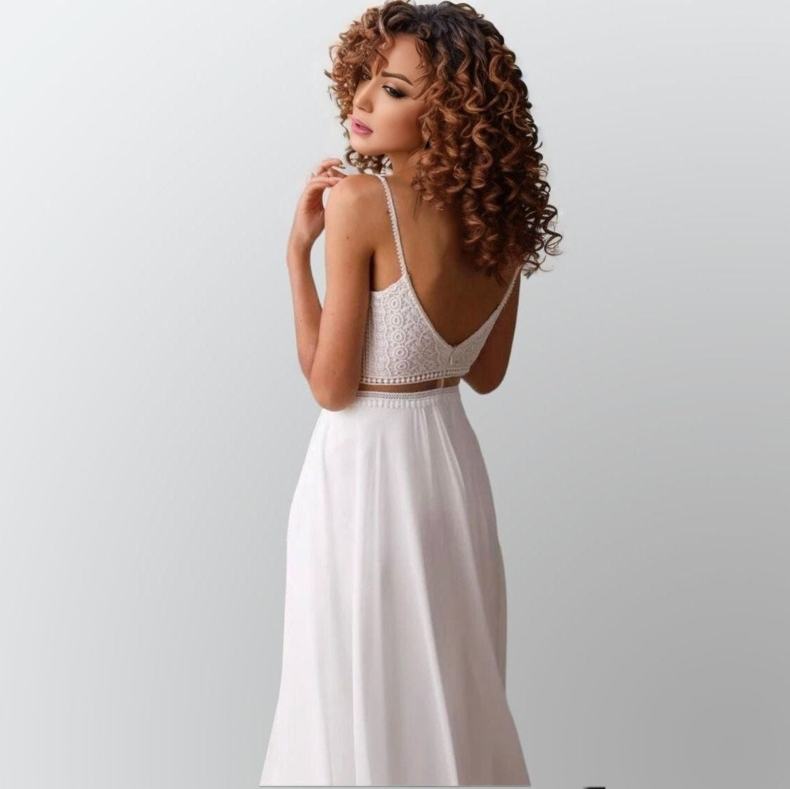 Model showcasing a bohemian wedding dress from back with a chiffon skirt, lace top, and geometric lace accents, offering the illusion of a two-piece design.