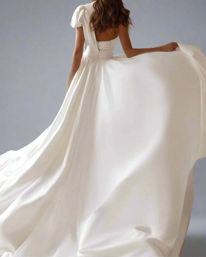 Elegant satin overskirt flowing behind the bride with one-shoulder asymmetrical bow detail on the Brylee dress.