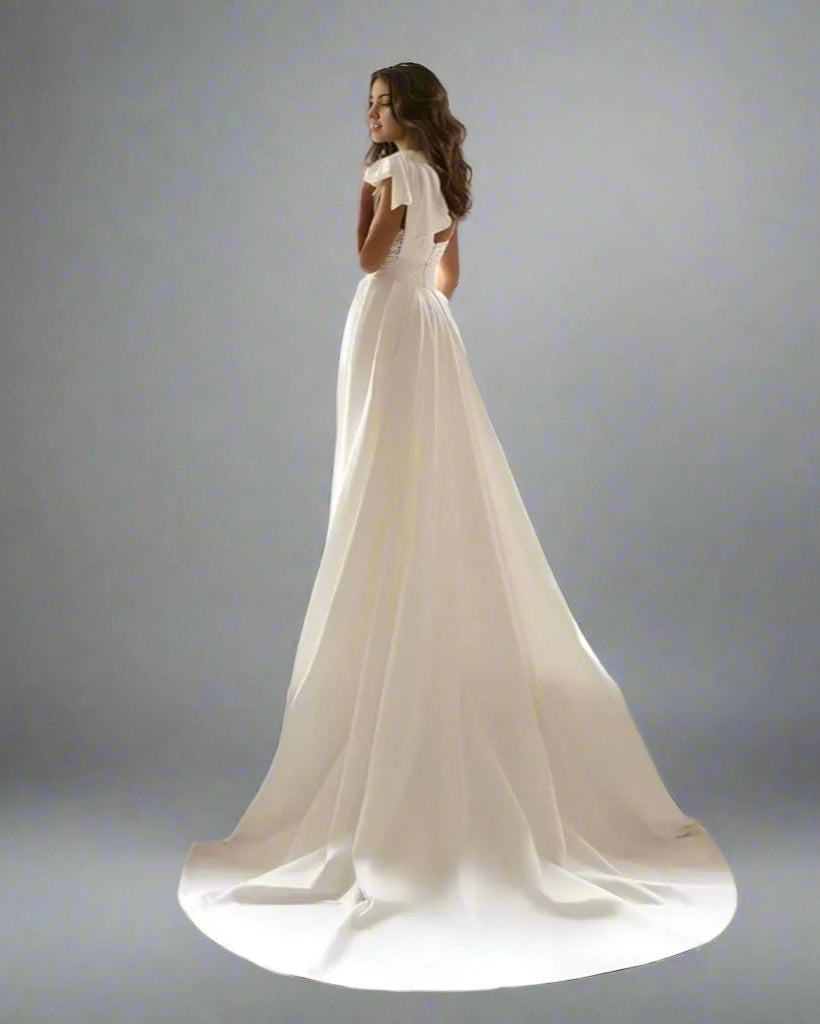 Bride posing in elegant wedding gown with asymmetrical one-shoulder detachable overskirt.