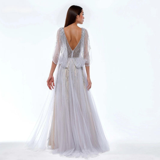 Woman wearing a white beaded sparkling dress with a backless design on a white background