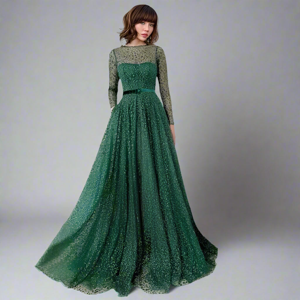 Woman wearing LIVIA emerald green gown with glitter lace and long sheer sleeves.