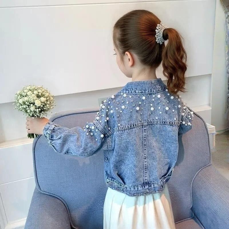 Child wearing a blue denim jacket with pearl embellishments, standing on a couch holding flowers.