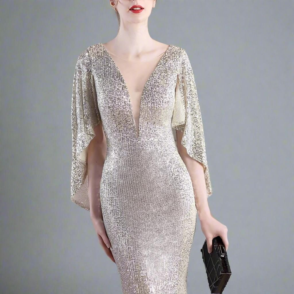 Woman wearing a sparkly silver dress with cape sleeves against a gray background