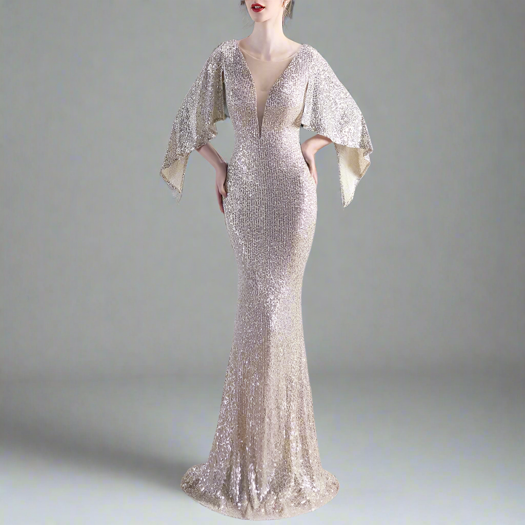 Model wearing elegant silver evening gown with cape sleeves on a gray background