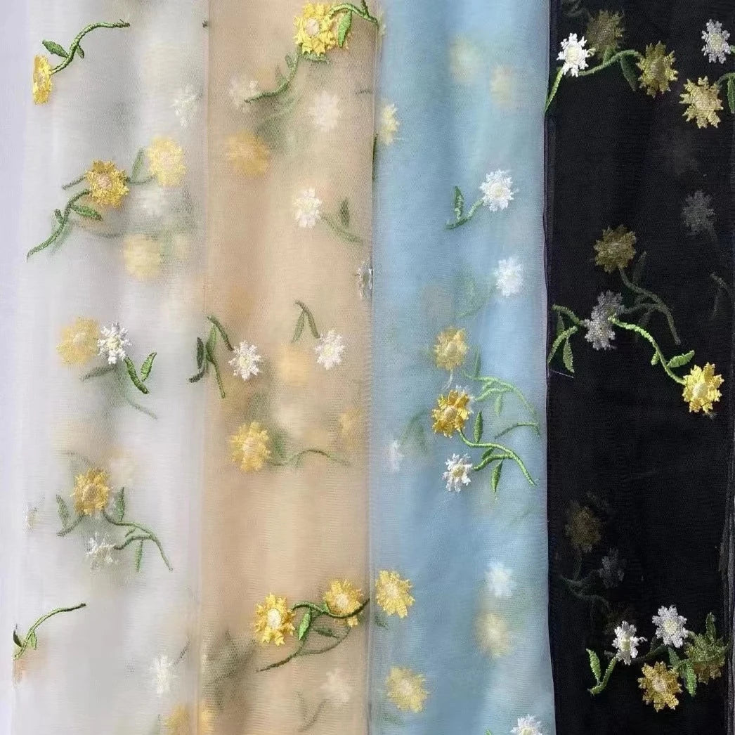 Detail of floral embroidered fabric in white, beige, light blue and black.