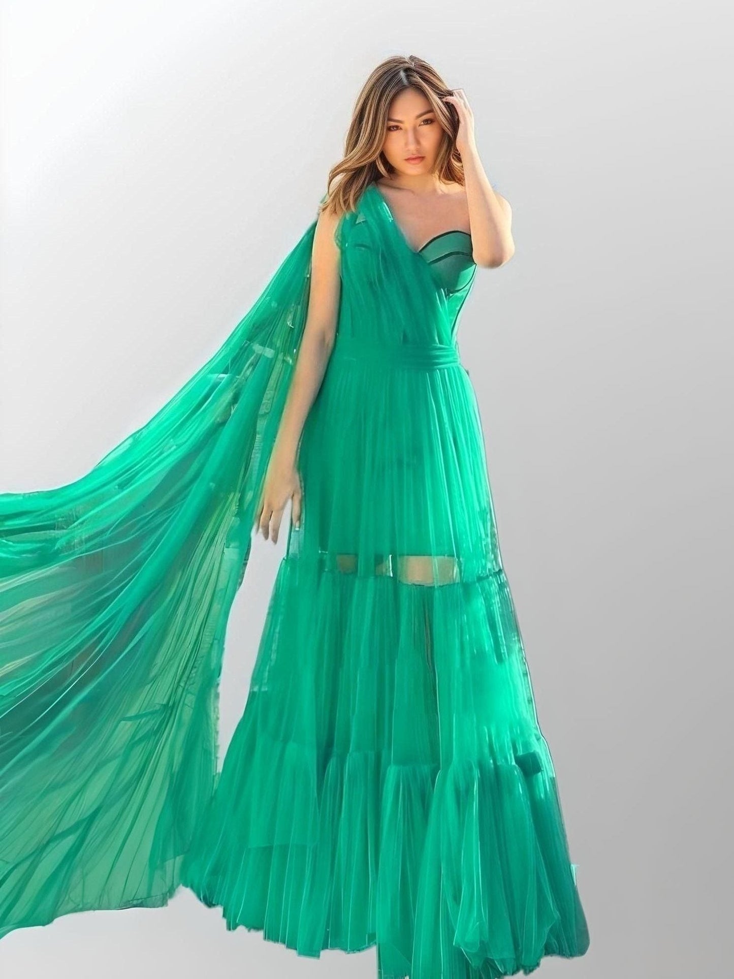 Woman wearing a green one-shoulder prom dress with ruffled tulle.