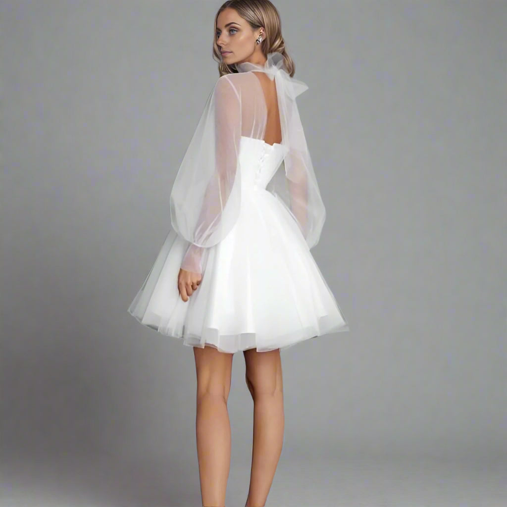 Woman posing in short elopement dress with long puff sleeves, open back with mesh bow on back.