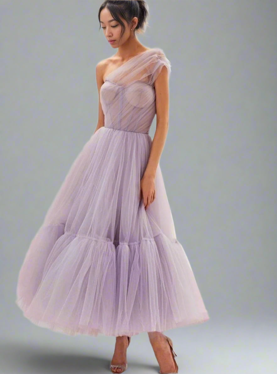 Model posing in lavender colored Skylar dress, emphasizing the one-shoulder design, fitted bodice and tiered tulle skirt.