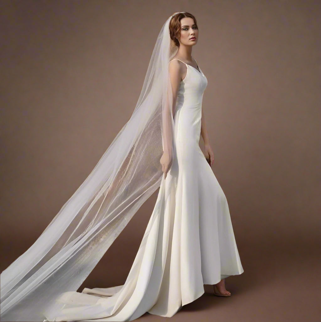 Bride posing with long bridal veil in white with cut edge design, draping gracefully behind her.