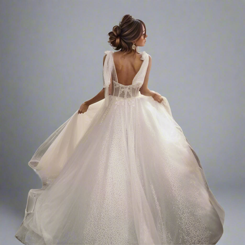 Back view of open-back wedding dress with fitted bodice and bow-tied straps, with flowing glitter skirt.