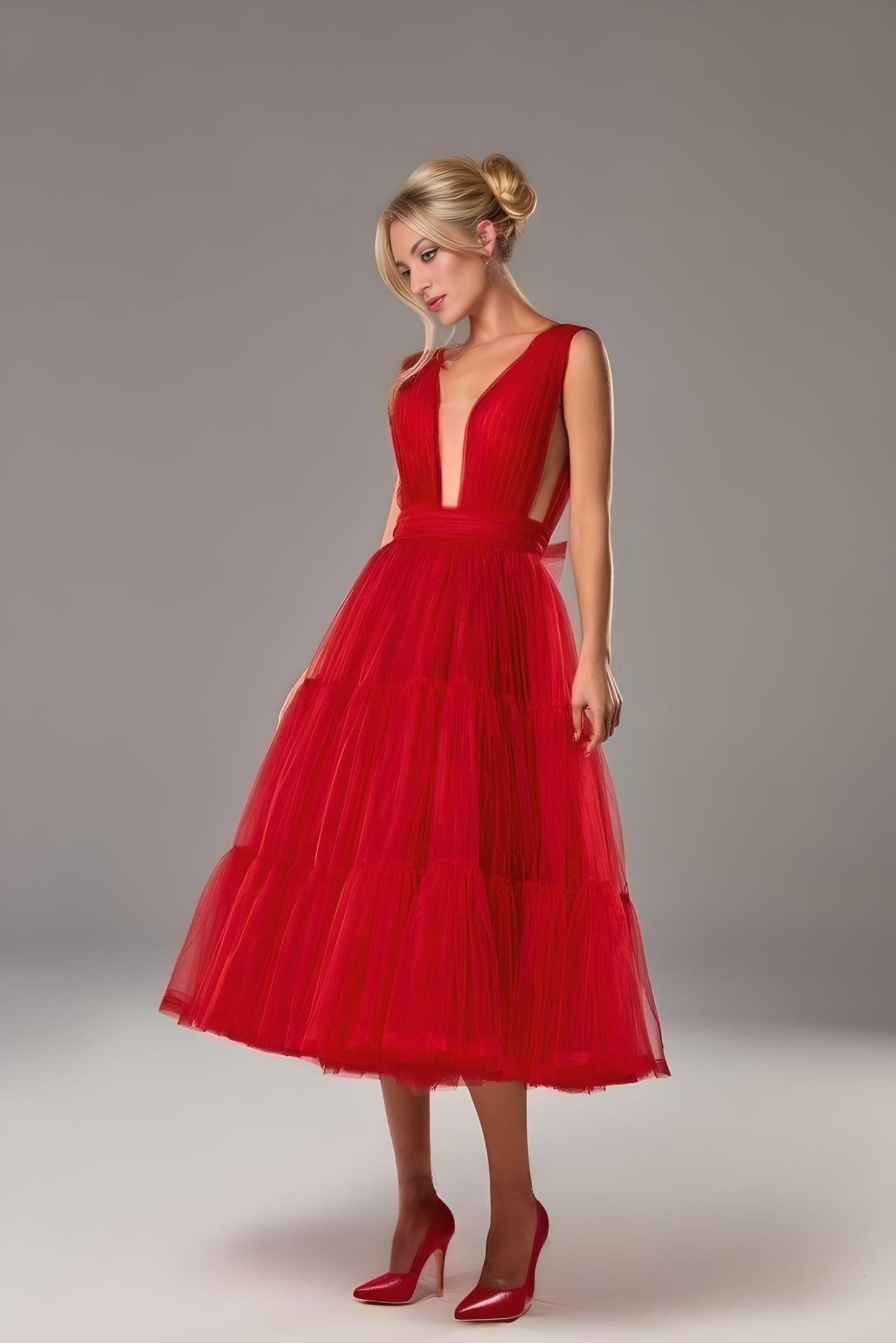 Woman posing in a red backless formal gown showing midi tiered length and side cut out.