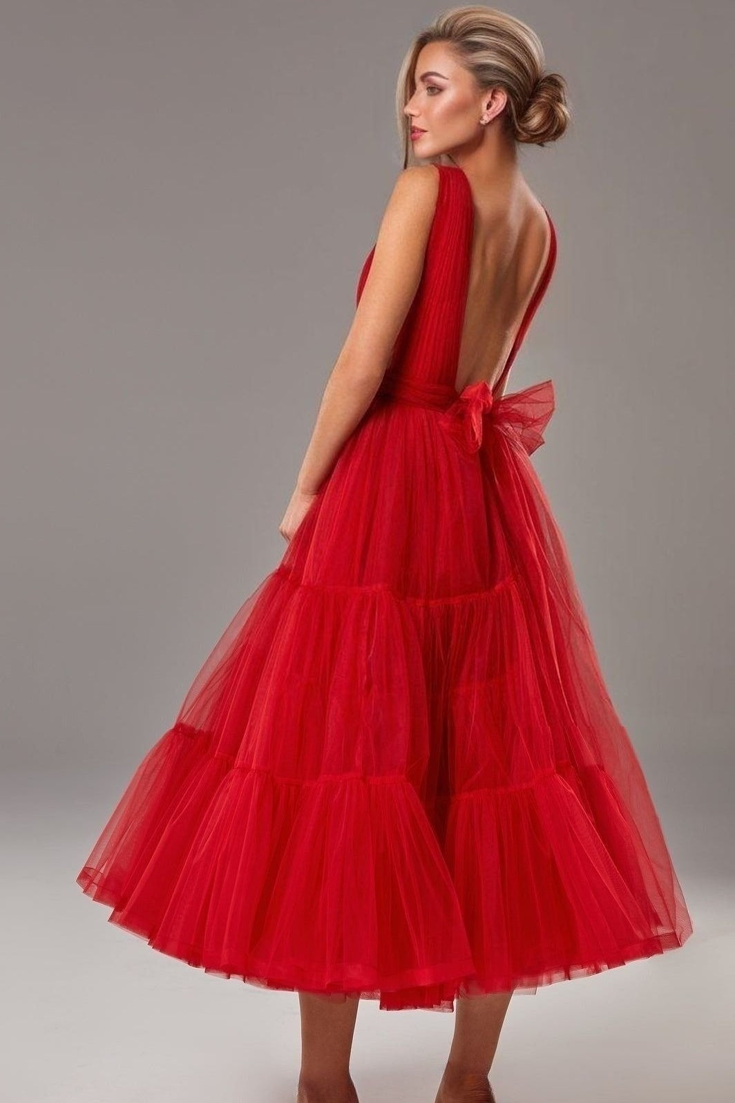 Woman posing in a bold red classic backless midi formal gown with back bow.