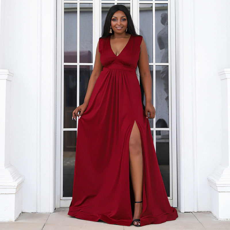 Model showcasing a plus-size burgundy gown with a pleated empire waist, deep V-neckline, and high slit, ideal for formal events or prom.