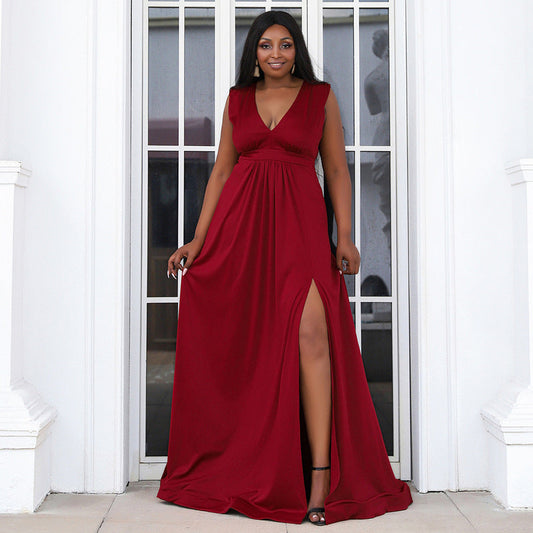 Model showcasing a plus-size burgundy gown with a pleated empire waist, deep V-neckline, and high slit, ideal for formal events or prom.