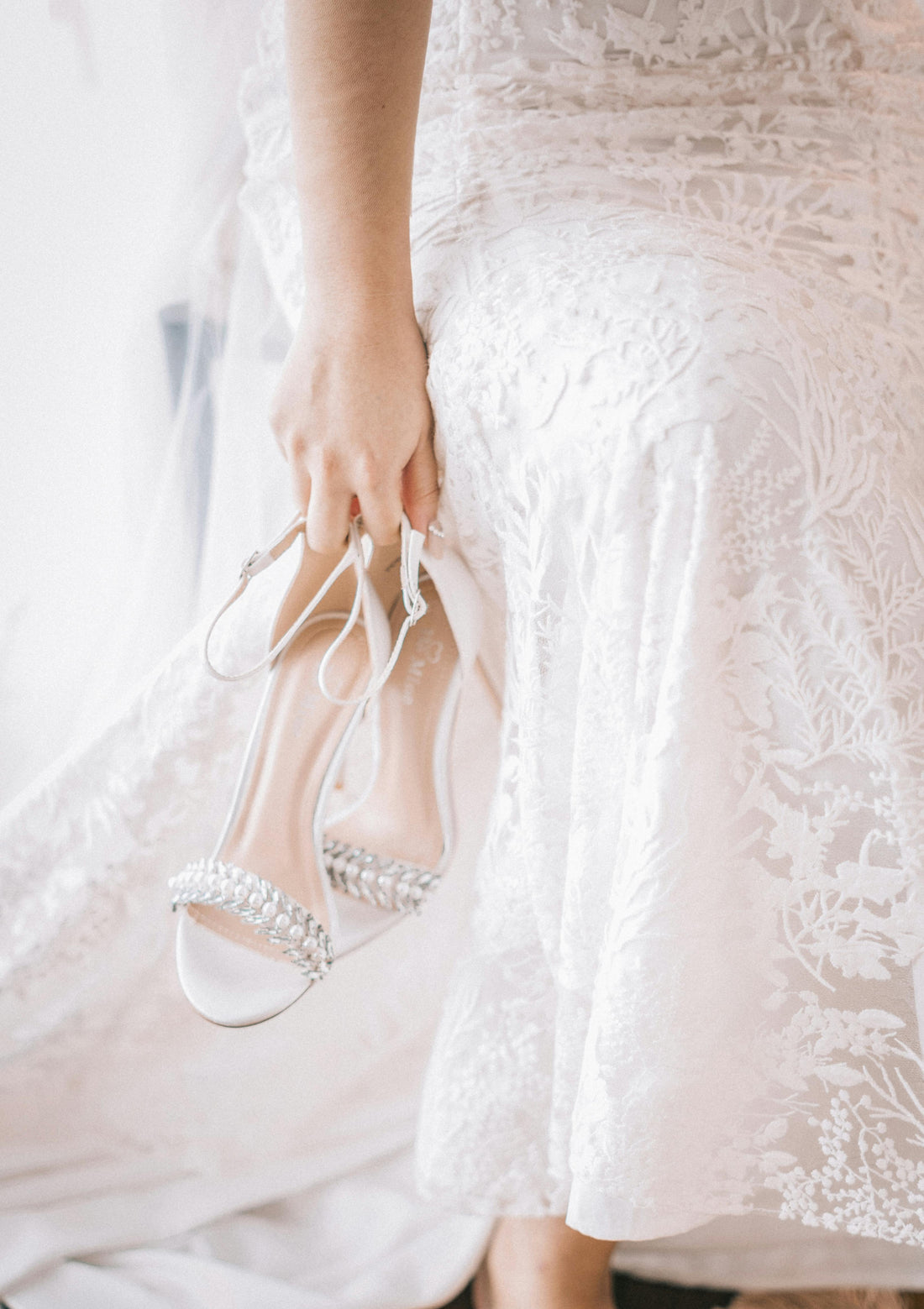 Bride holding her shoes and showing detail of her wedding dess lace