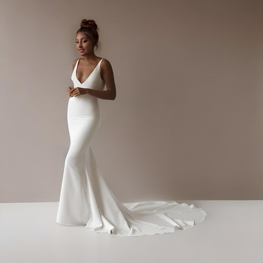 Model in a minimalist mermaid gown with a plunging back, backless design, and delicate back buttons.