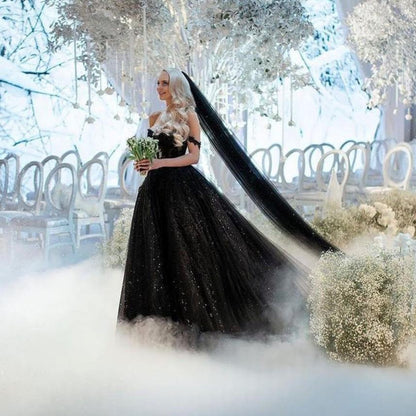 Bride in black sparkling gown and long black veil flowing behind her walking down the aisle holding flowers.