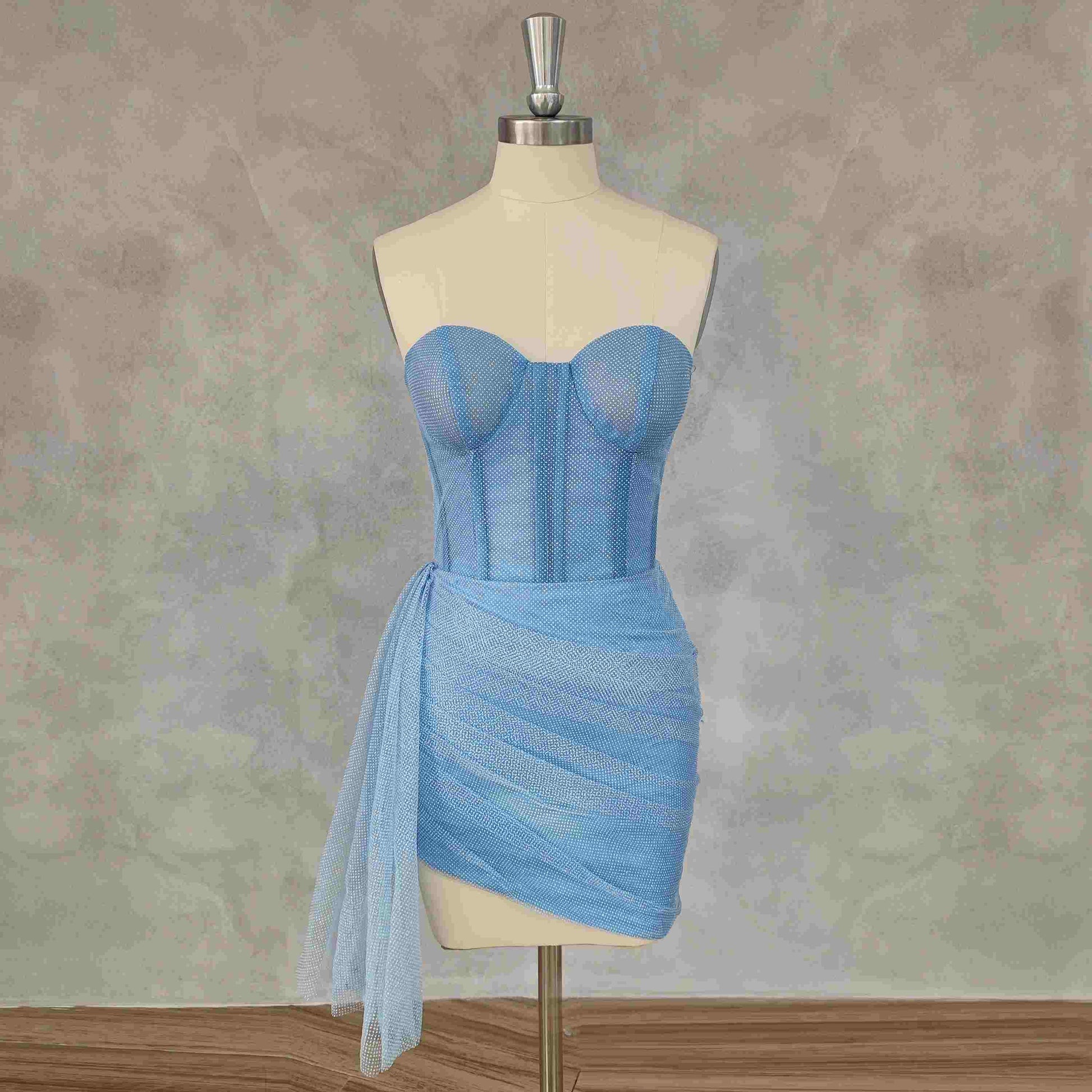 A model of the JULIETTE Mini Formal Dress, highlighting the structured bodice with boning and pleated, asymmetrical skirt.
