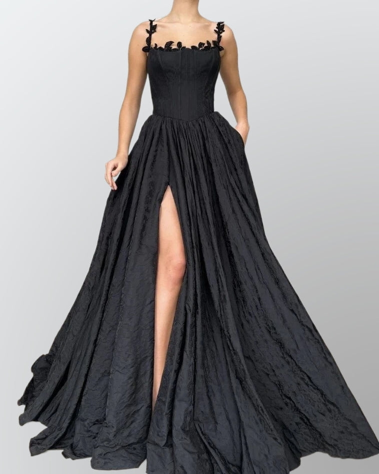 Bride wearing a black satin wedding gown featuring lace appliques, a bold side slit, and delicate spaghetti straps.

