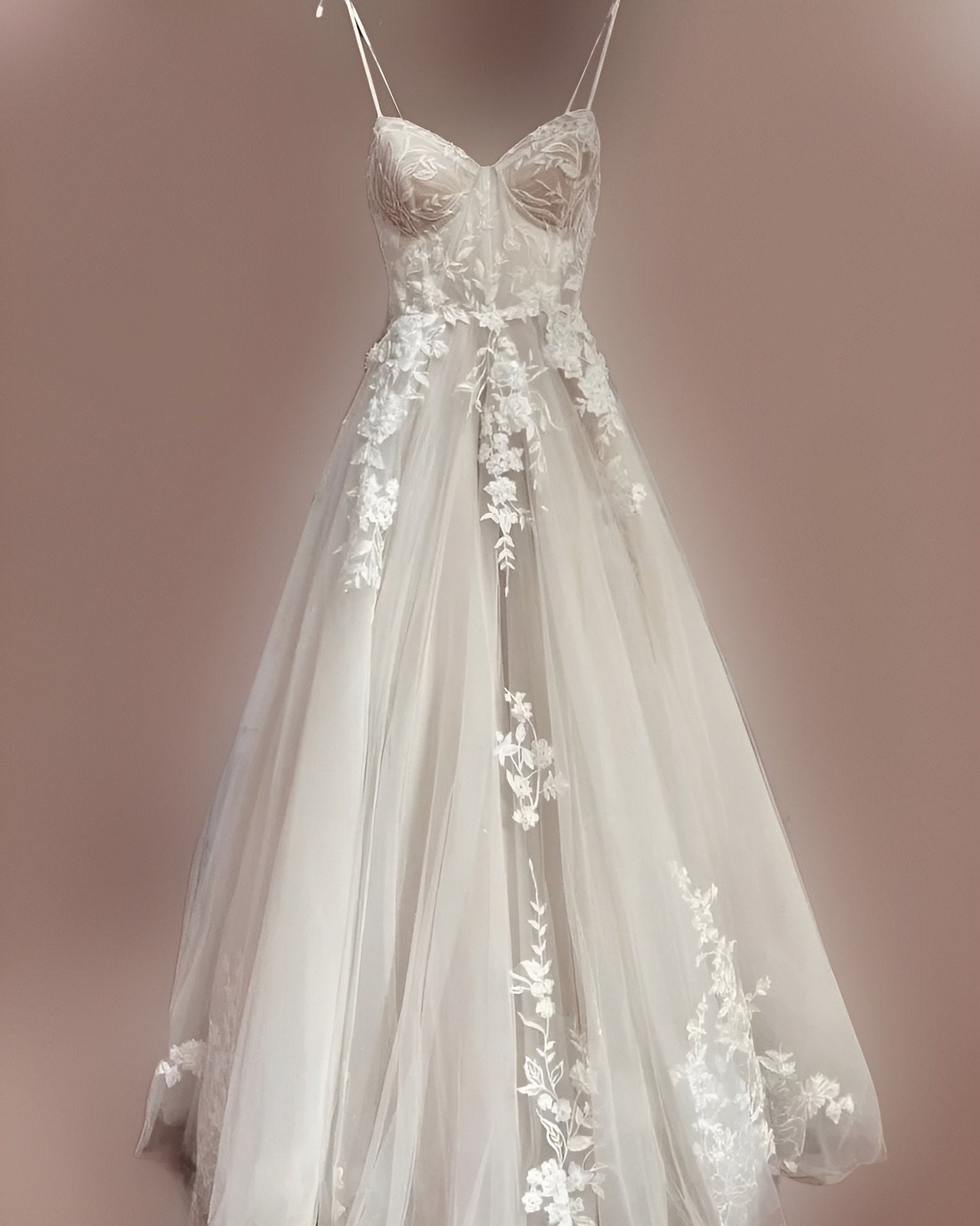 The LEONA wedding dress displayed on a hanger, highlighting its beautiful champagne lace and spaghetti straps in an elegant front view.