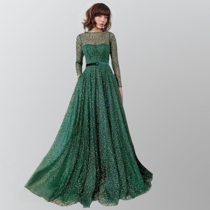 Woman wearing LIVIA emerald green gown with glitter lace and long sheer sleeves.