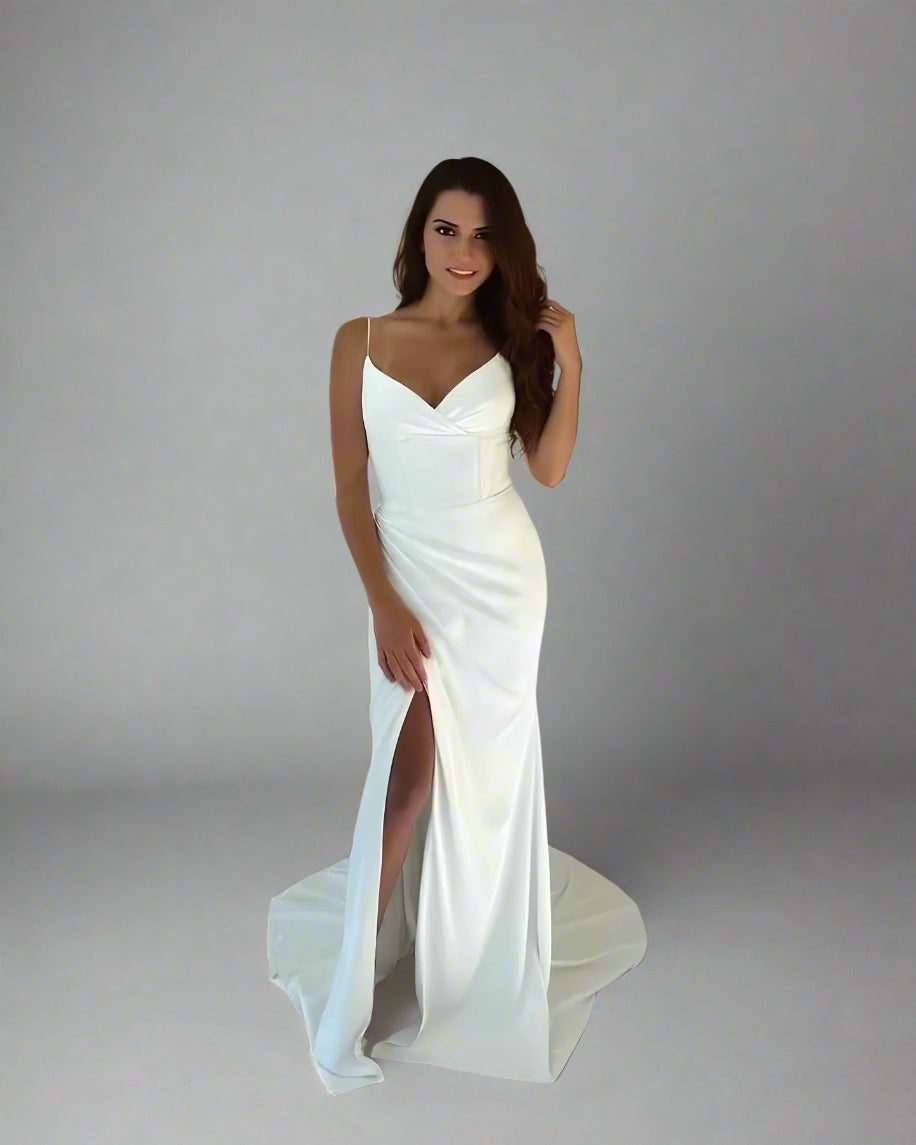 Woman wearing a white wedding dress with a slit on a plain background