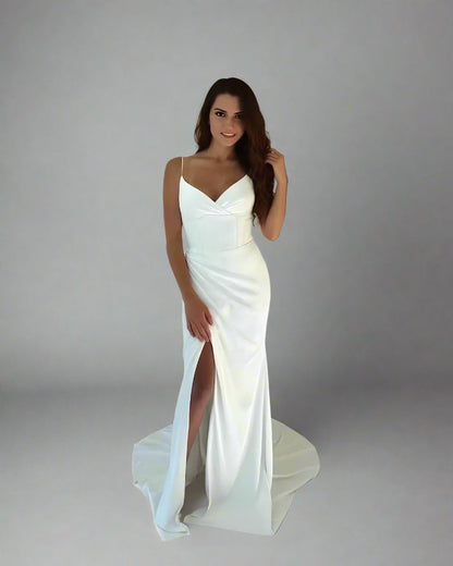 Woman wearing a white wedding dress with a slit on a plain background
