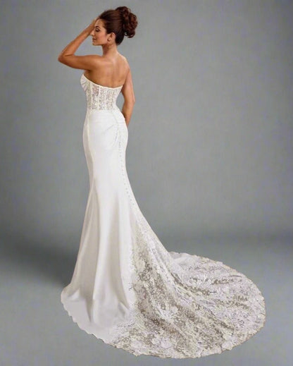 Woman wearing a white wedding dress with a long lace train on a gray background