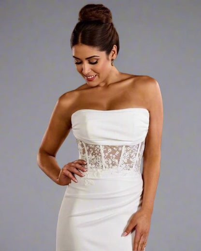 Woman wearing a white strapless dress with lace detailing in an indoor setting.