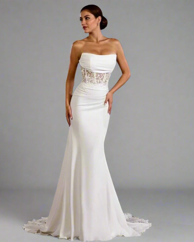 Woman wearing a strapless white wedding dress with lace detailing on a gray background