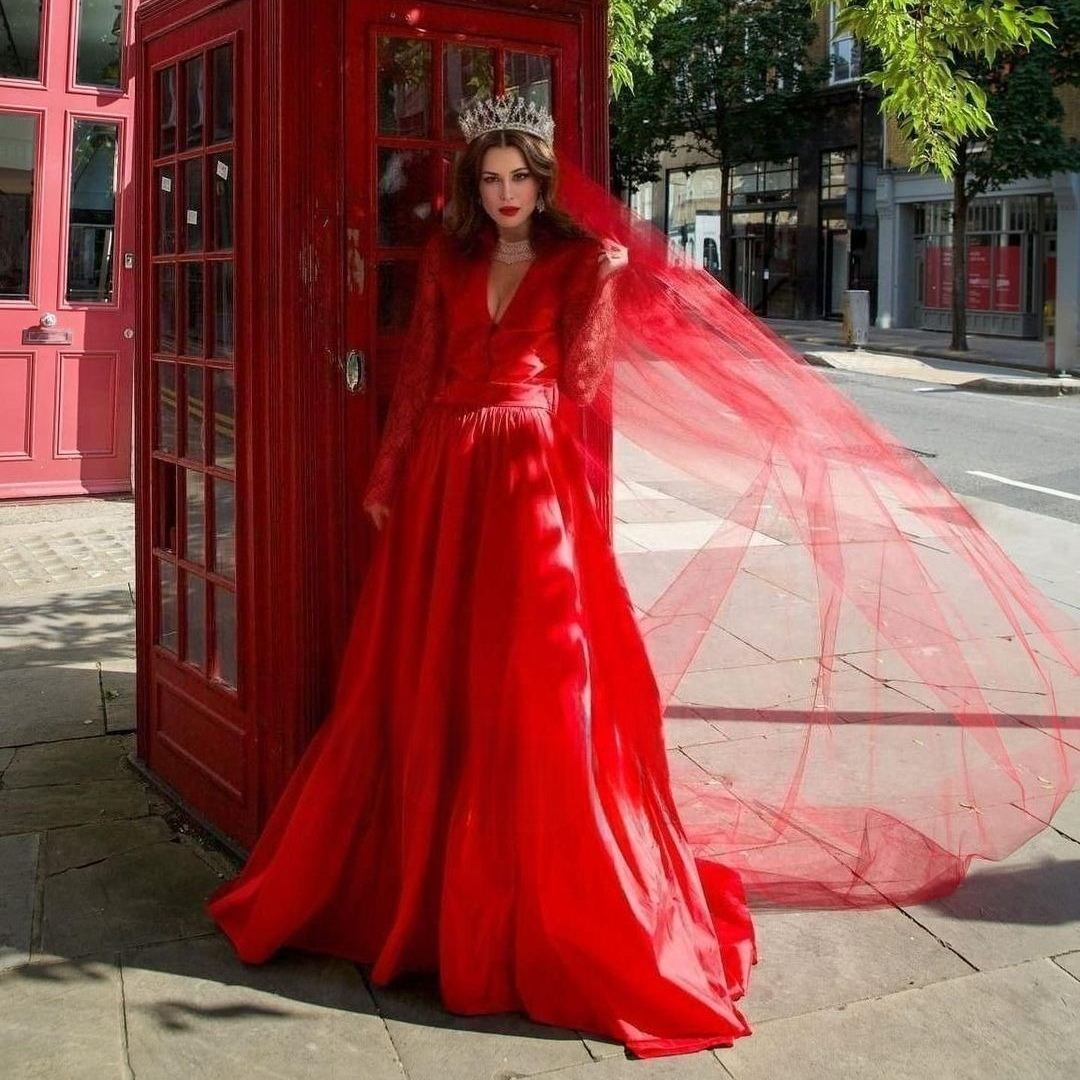 A bride in red Wedding Dress wearing the Red Wedding Veil and crown, highlighting its vibrant color and elegant flow, standing in front of typical english phone booth.