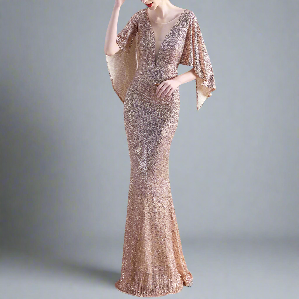 Woman wearing gold sparkly evening gown with cape-like sleeves.