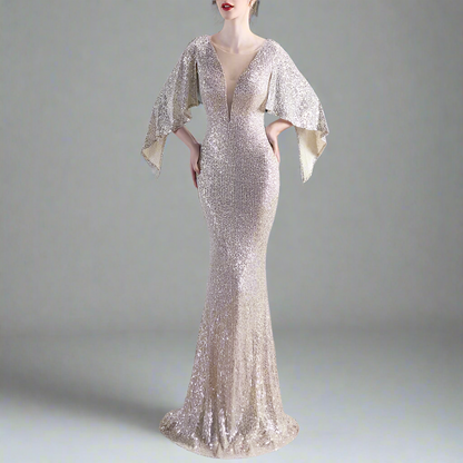 Model wearing elegant silver evening gown with cape sleeves on a gray background