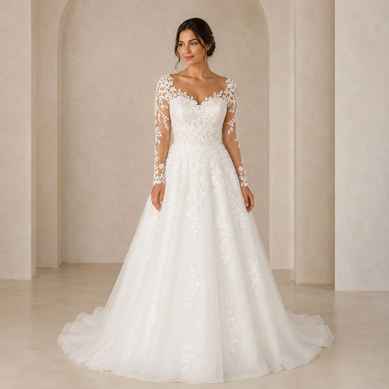 A woman modeling a long-sleeve white wedding gown with floral lace embroidery, standing in a softly lit beige interior with arched walls.