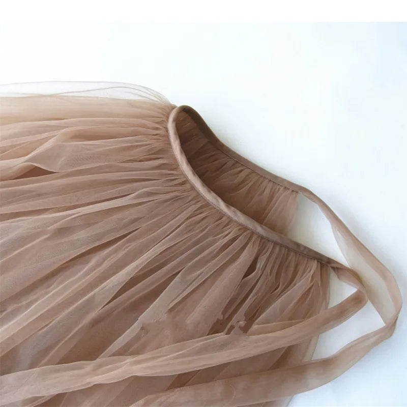 A close-up of a sheer tulle tutu skirt in a muted taupe-brown color, showing the gathered waistband and thin straps against a plain white background.