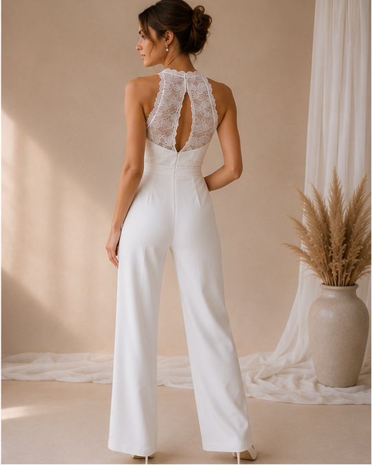 Woman wearing a white lacetop  jumpsuit with flowy pants in a softly lit room.