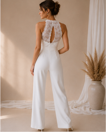 Woman wearing a white lacetop  jumpsuit with flowy pants in a softly lit room.