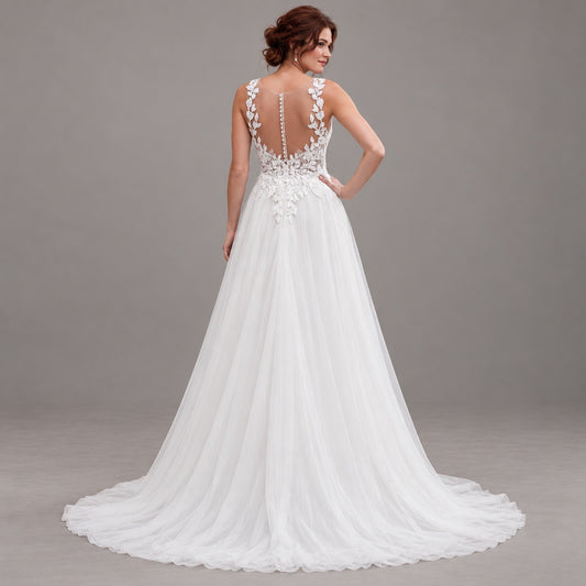 A woman modeling a white wedding gown from the back, showing a deep V-back with floral lace applique, a beaded waistband, and a full tulle train against a neutral gray studio background.