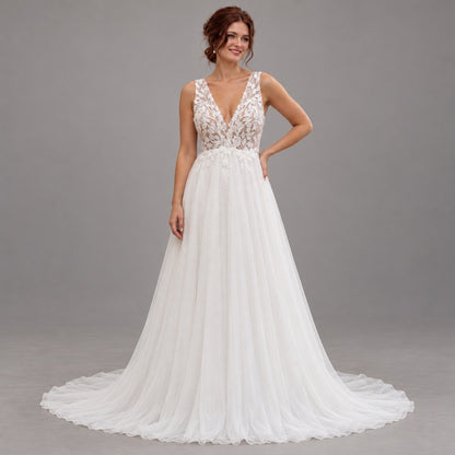 A woman modeling a white wedding gown with a lace V-neck bodice, sheer straps, and a full tulle skirt with a train, photographed against a plain gray studio background.