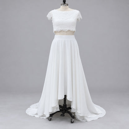 White two-piece formal gown displayed on a dress form mannequin against a neutral gray studio background. The outfit features a short-sleeve lace crop top with scalloped edges and a high-waisted, flowing chiffon maxi skirt with a slight train.